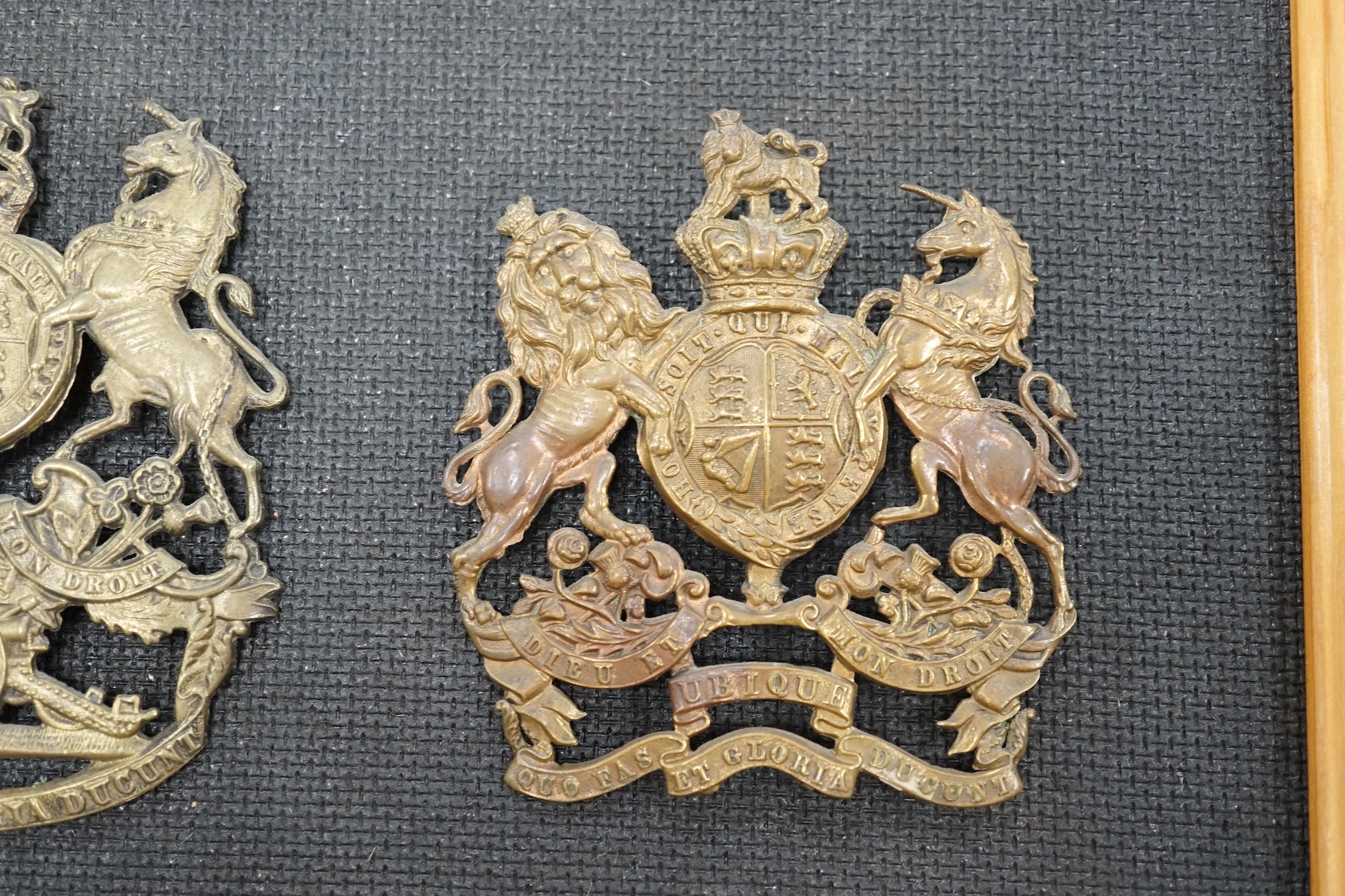 Two Royal Artillery brass helmet plates, one with three lugs and the other with two lugs, loosely mounted onto a backing board. Condition - fair to good, top lug missing to one